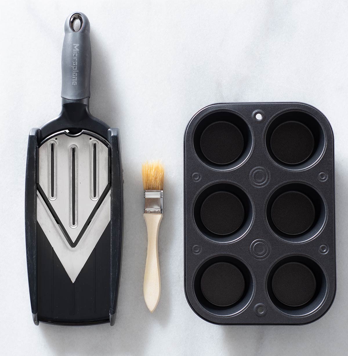 A mandoline, a brush and a muffin pan.