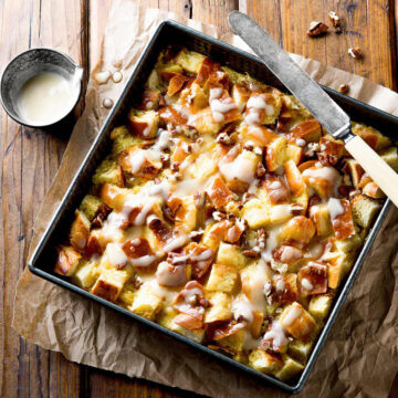 Maple pecan bread pudding with sauce in a square baking pan.