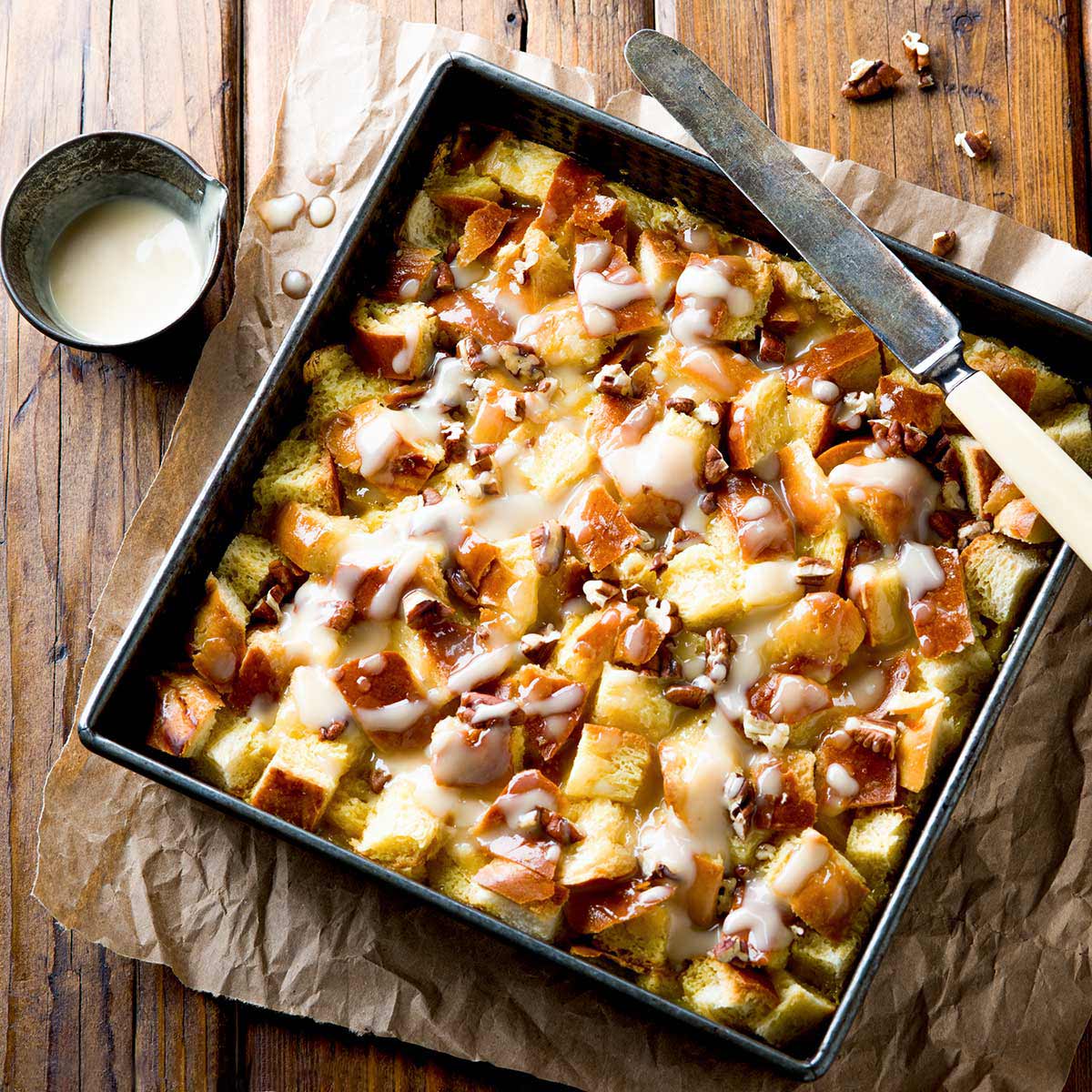 Maple pecan bread pudding with sauce in a square baking pan.