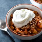 Apple crisp with whipped cream in a bowl.