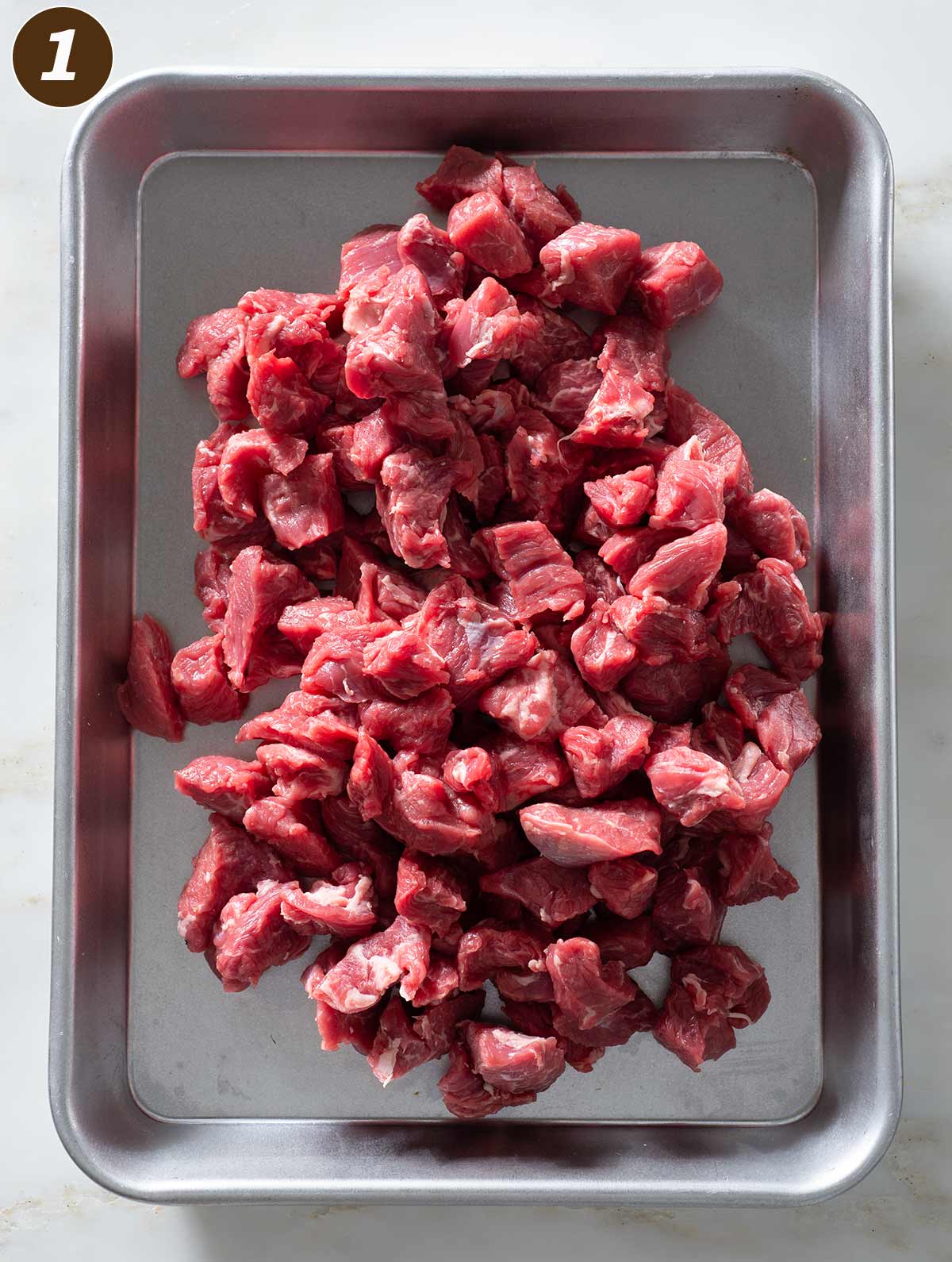 Raw chuck beef chunks on a metal tray.