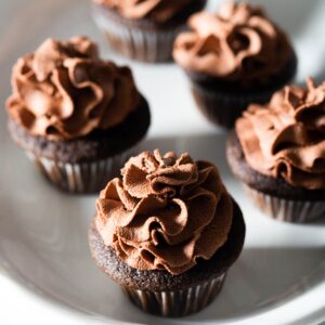 Five mini chocolate cupcakes on a white platter.