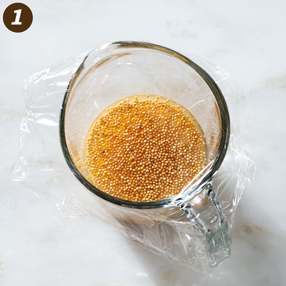 Mustard seeds and liquid in a glass measuring cup.