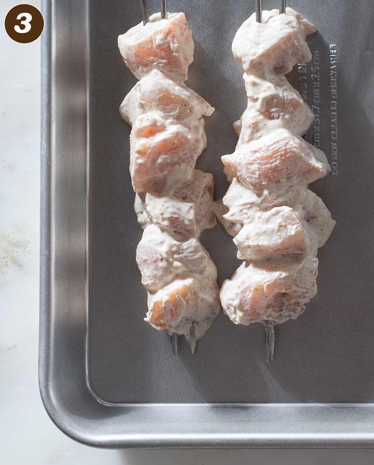 Marinated raw chicken on skewers on a baking sheet.