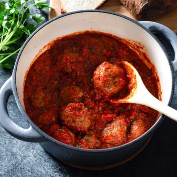 Meatballs and marinara sauce in a pot with a spoon.