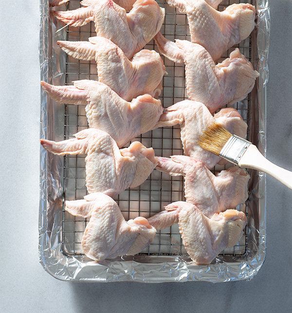 Raw chicken wings being brushed with oil.