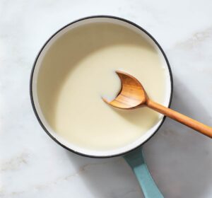 Cream and melted white chocolate being stirred in a saucepan.