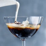 White Russian cocktail being poured into a glass.
