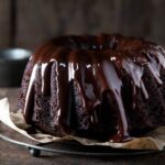 A glazed chocolate Bourbon cake on a round cooling rack.