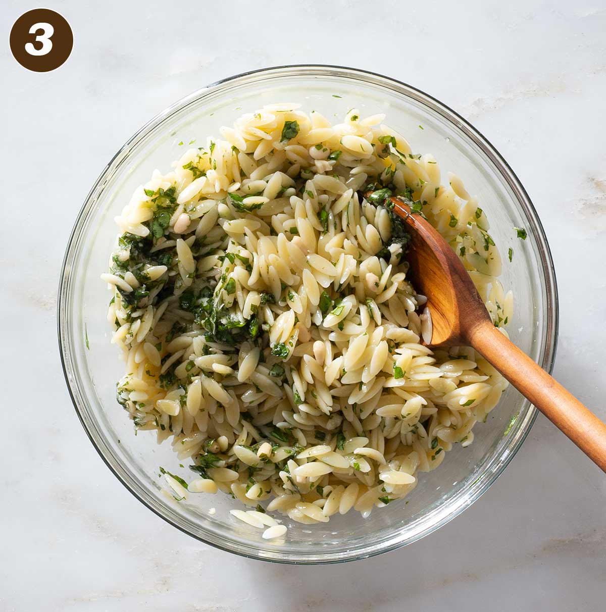 Orzo and pesto being mixed in a bowl.