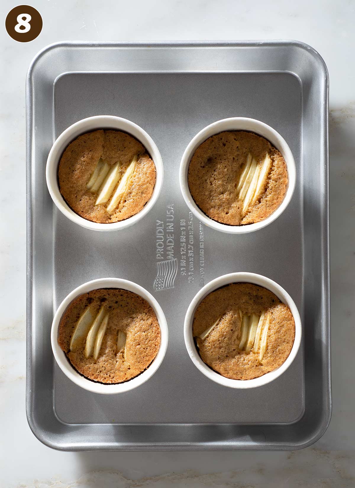 Four mini apple cakes in ramekins on a baking sheet.