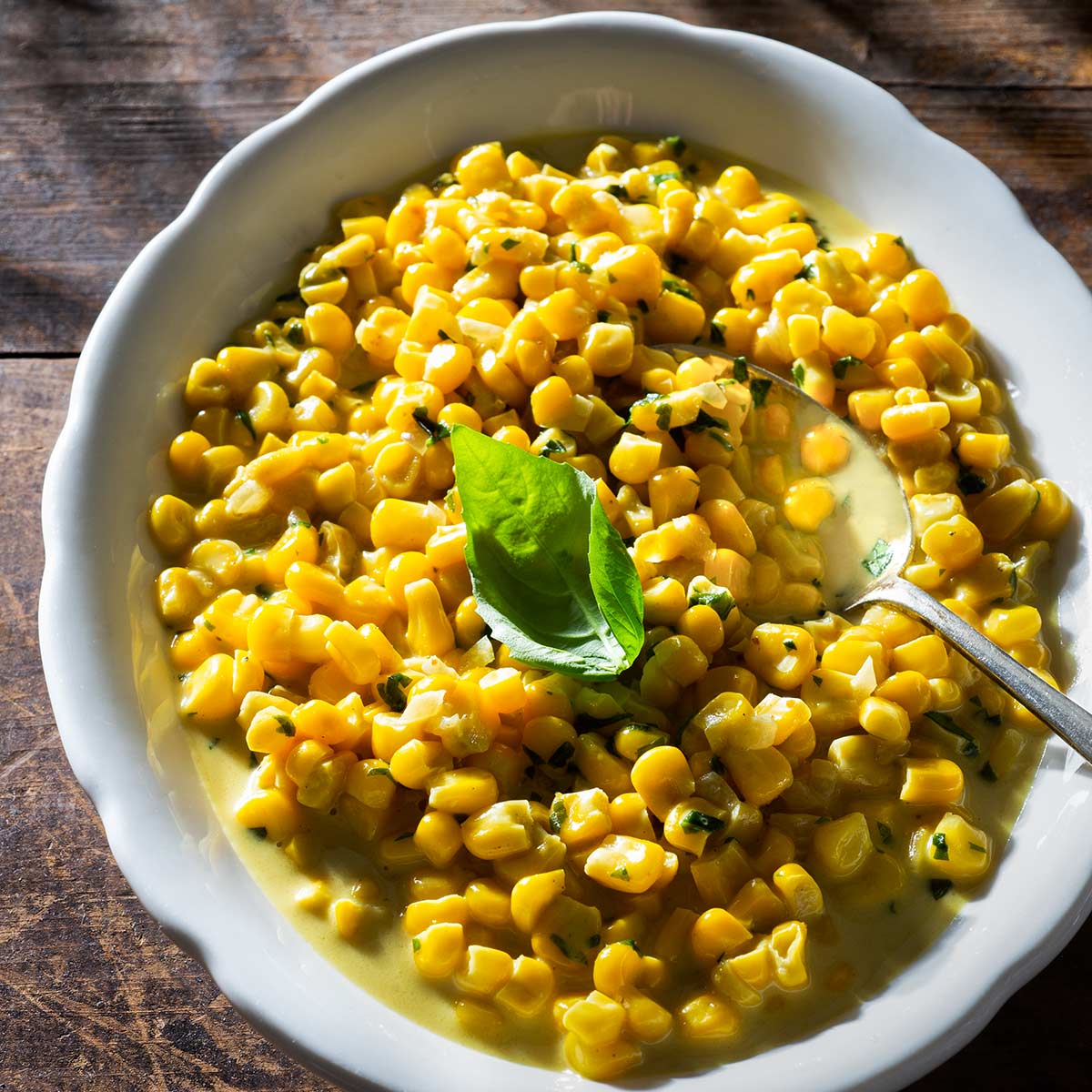 Curried corn on a plate with a spoon and fresh basil.