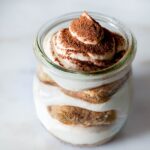 A small glass jar filled with a tiramisu trifle.