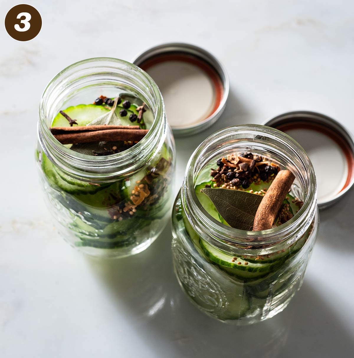 Two jars filled with cucumber slices and spices.