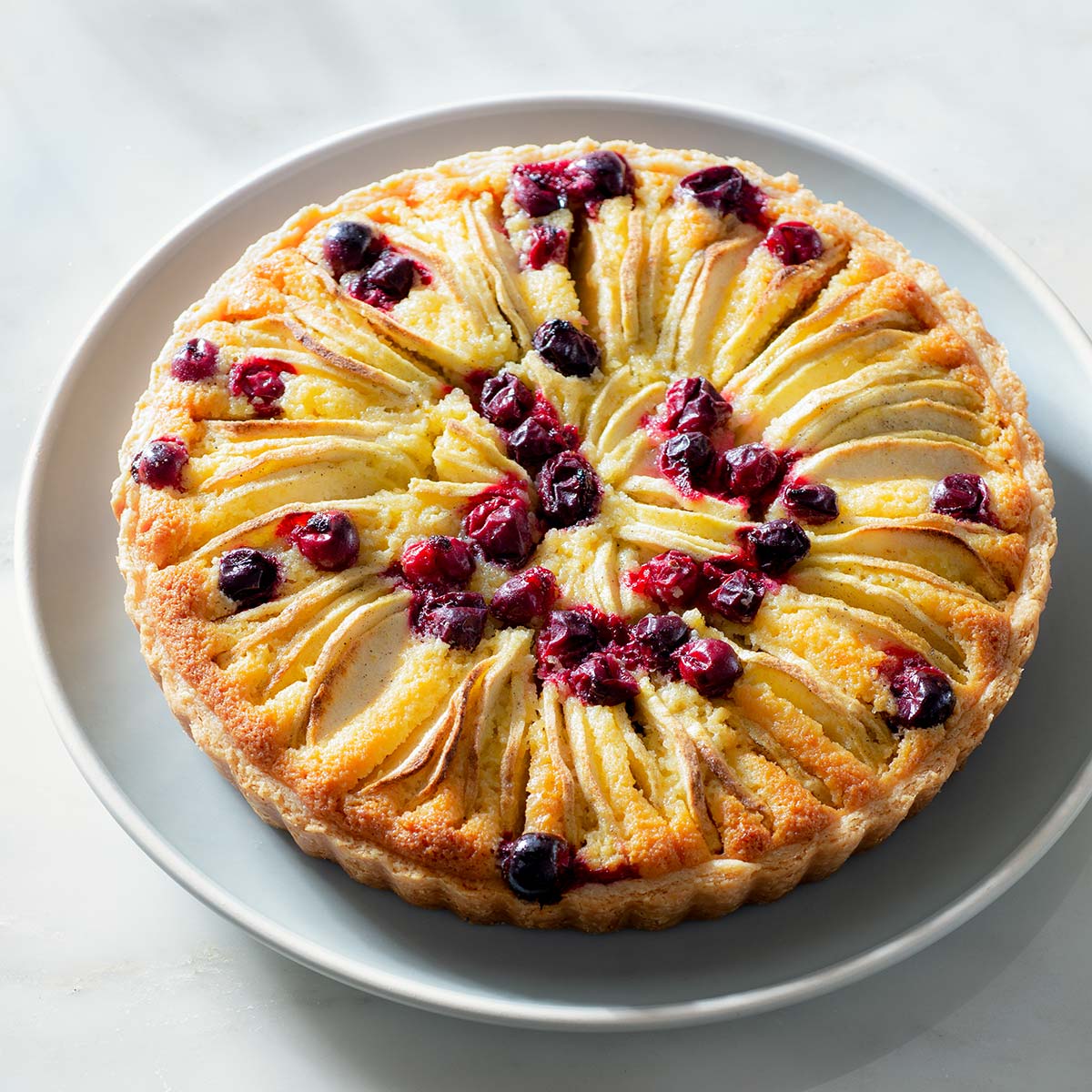 An apple frangipane tart with cranberries on a blue plate.