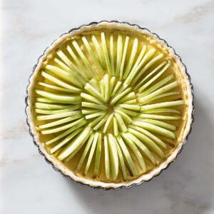 An unbaked apple frangipane tart on a kitchen counter.