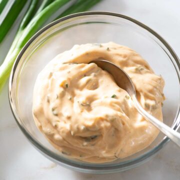 Scallion aioli with a spoon in a glass bowl.