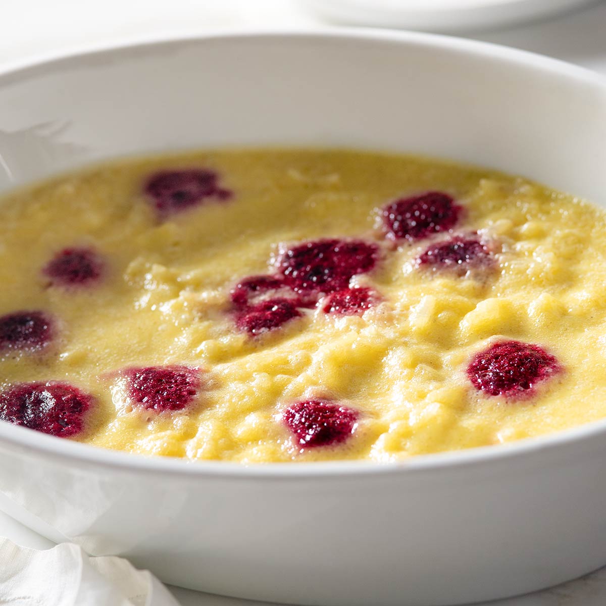 Baked custard rice pudding with raspberries in a baking dish.