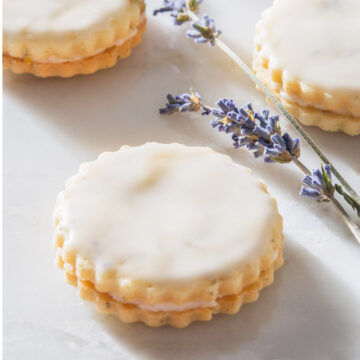 Lavender cookies with filling and icing on a table.