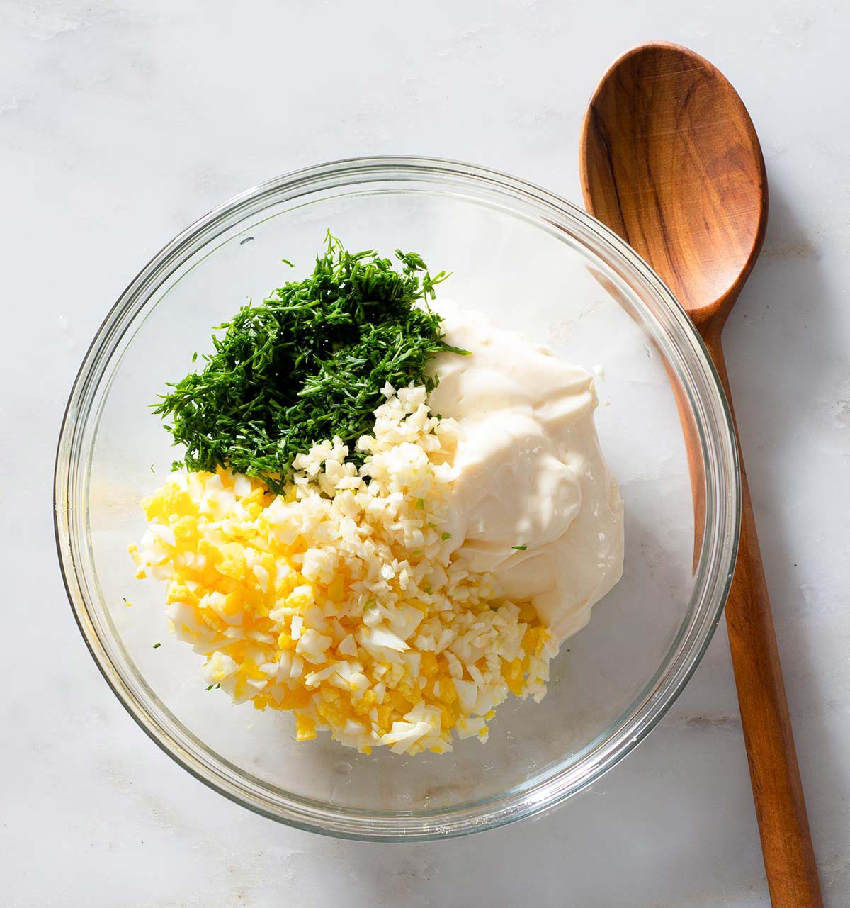 Dill aioli ingredients in a bowl and a wooden spoon.