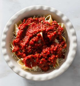 Meatball-stuffed shells topped with tomato sauce in a baking dish.