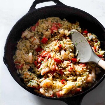 Orzo shrimp scampi in a skillet with a rubber spatula.