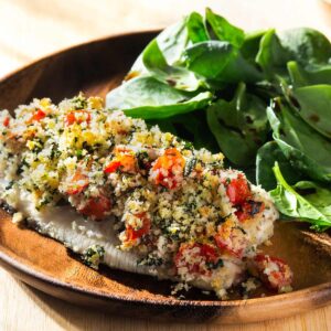 Baked bruschetta tilapia with spinach salad on a wooden plate.