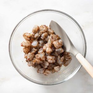 Raw shrimp being mixed with Jerk seasoning in a bowl.