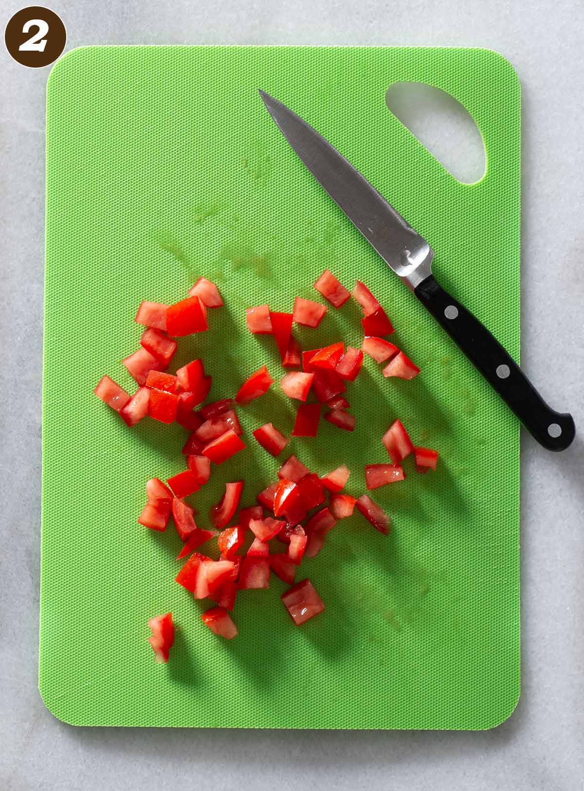 Diced tomato on a cutting mat with a knife.