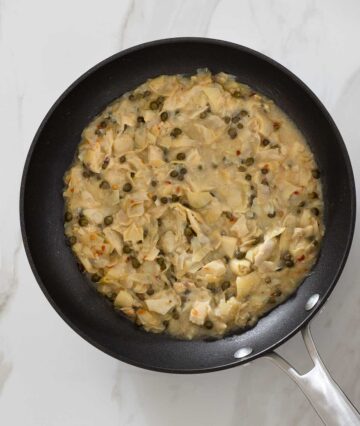 Artichoke piccata in a pan.