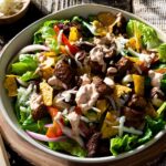 Steak fajita taco salad with dressing in a bowl.