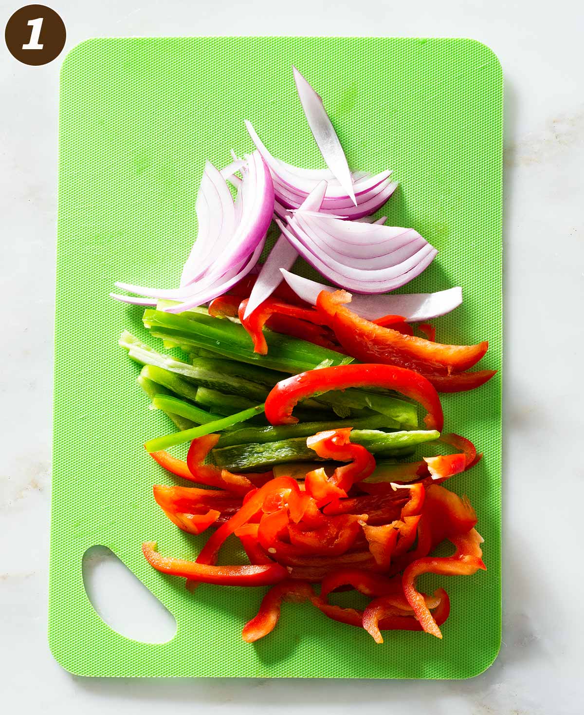 Sliced peppers and onion on a cutting mat.