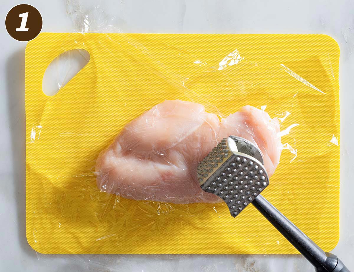 Raw chicken breast on a cutting mat with a meat mallet.