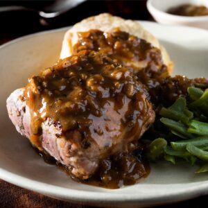 Pork tenderloin with sauce, beans and biscuit on a plate.