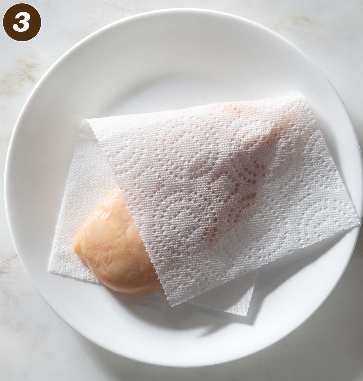 Chicken breast with paper towel on a plate.