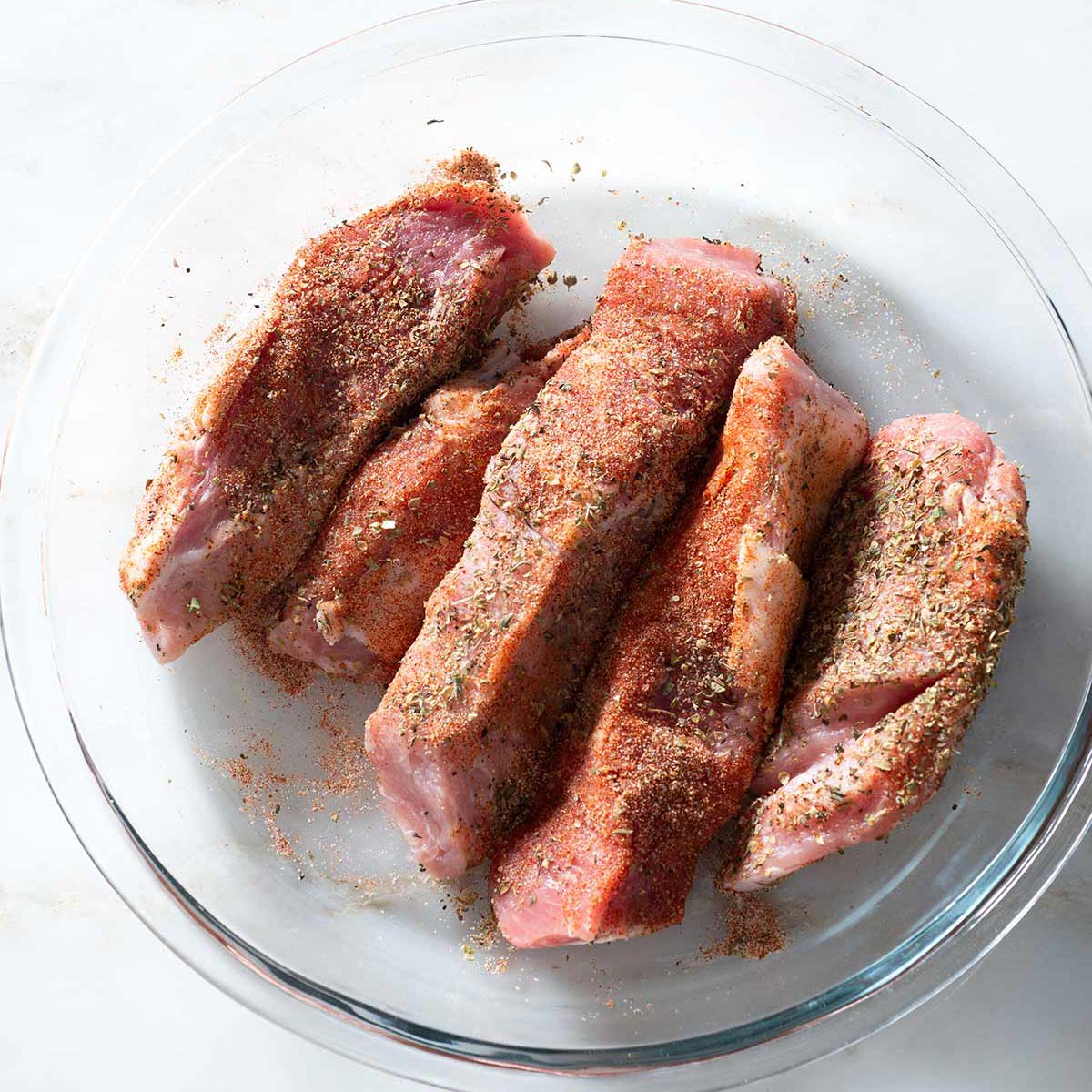Raw spice-rubbed boneless ribs on a glass plate.
