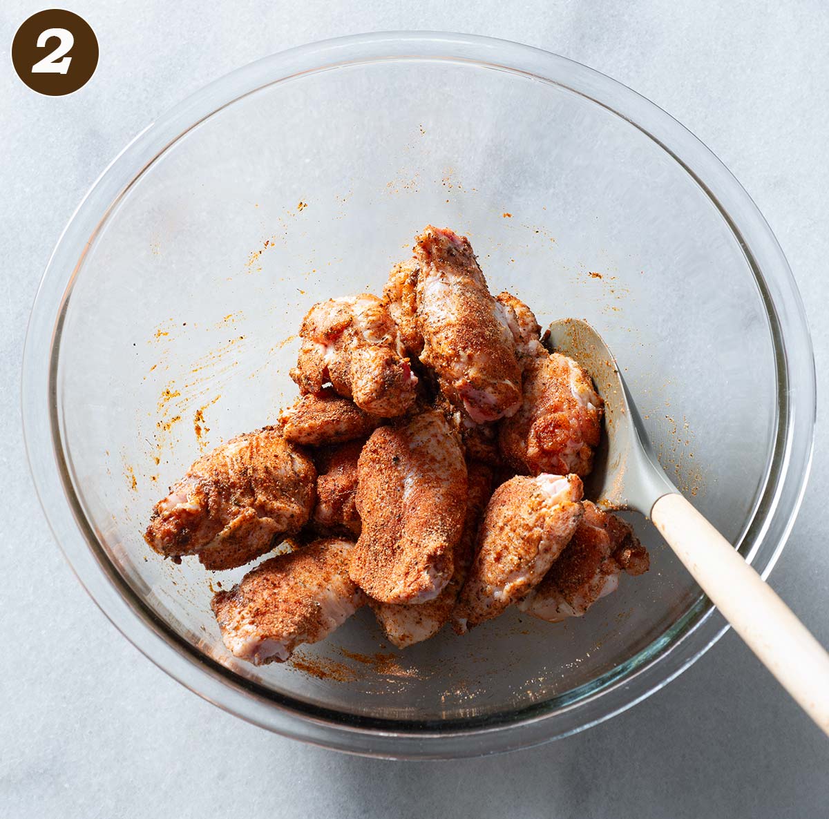 Chicken wings being tossed with seasoning in a bowl.