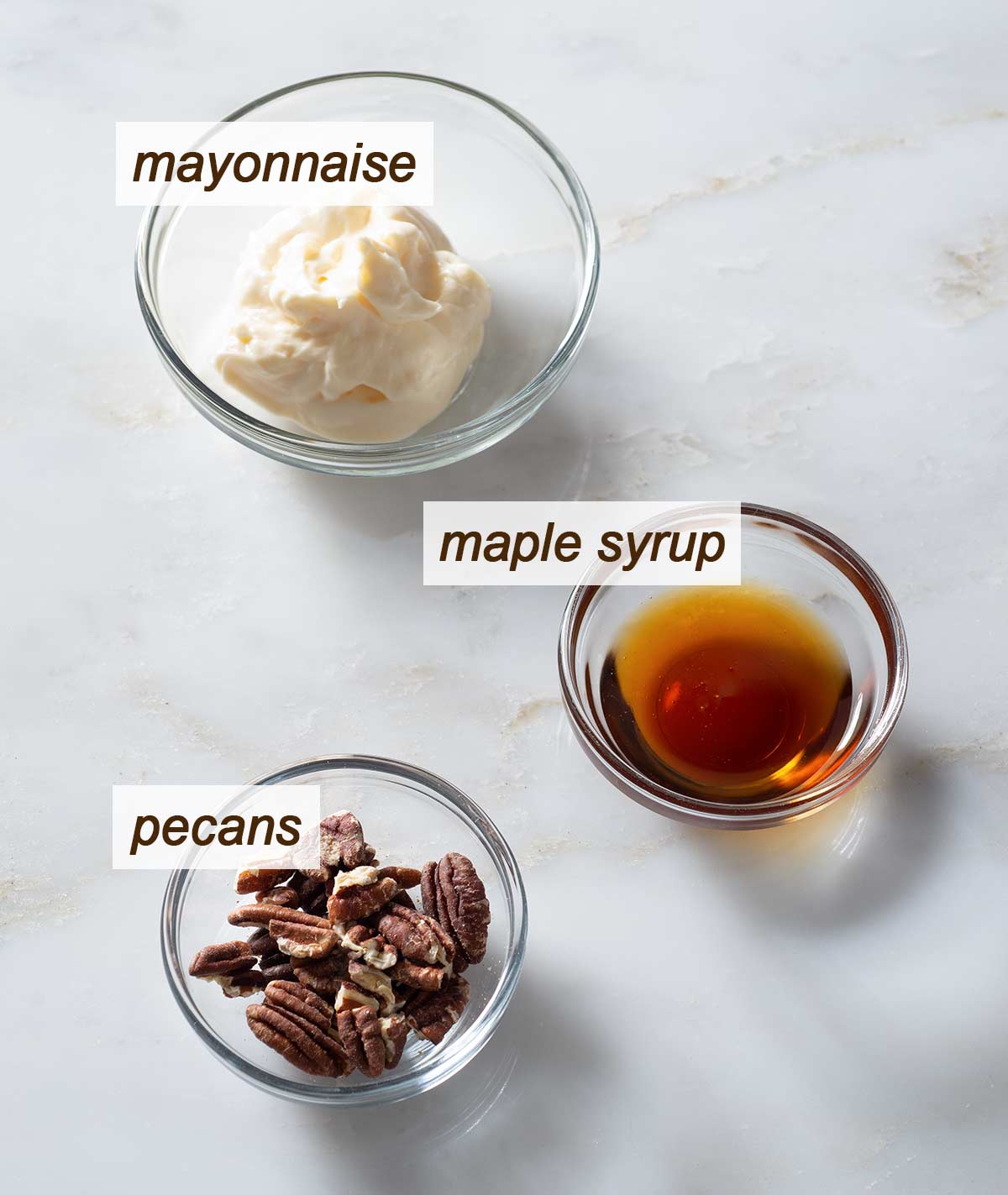 Maple syrup, pecans and mayonnaise in bowls on a table.