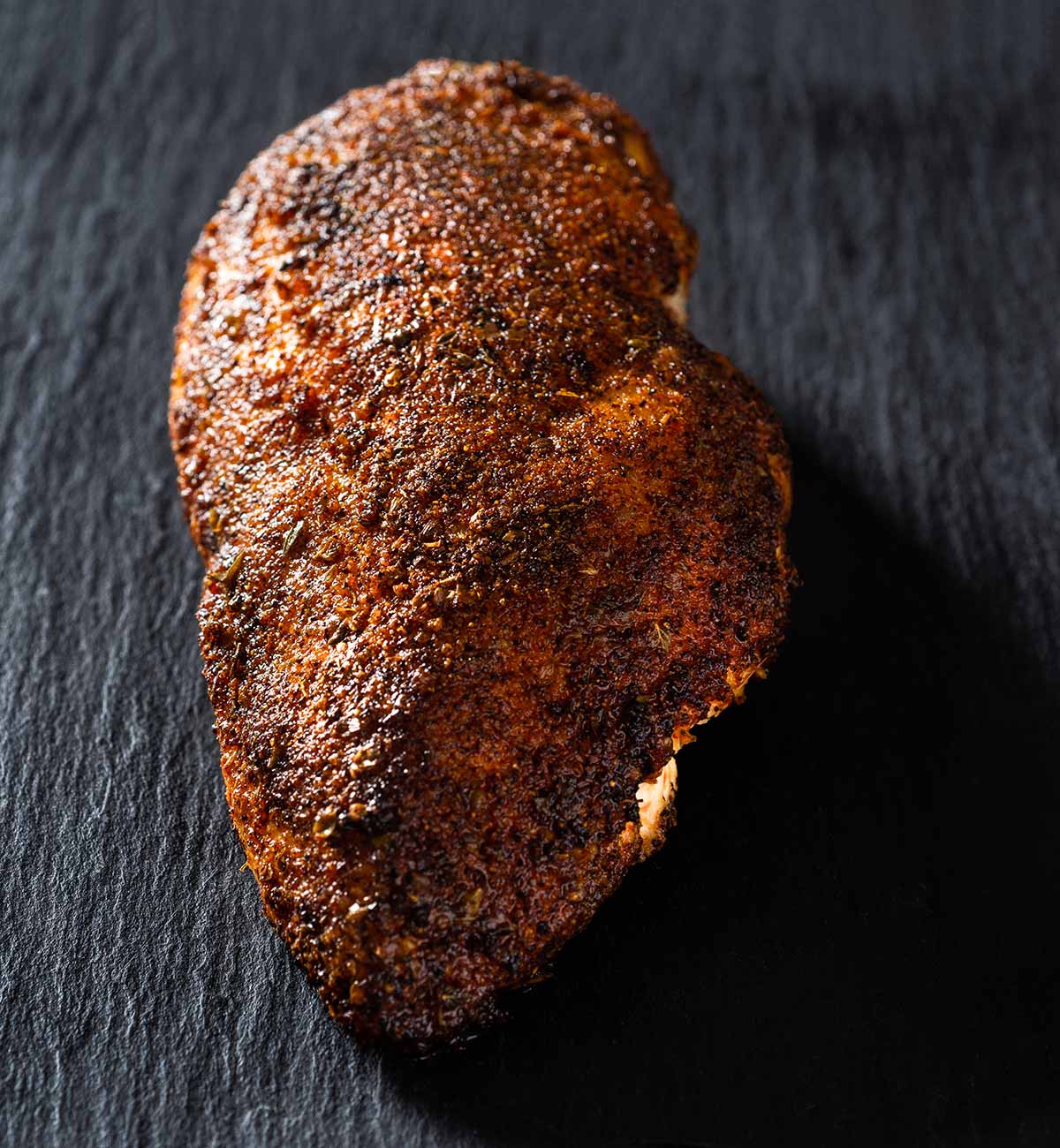 Spice-rubbed, cooked chicken breast on a cutting surface.