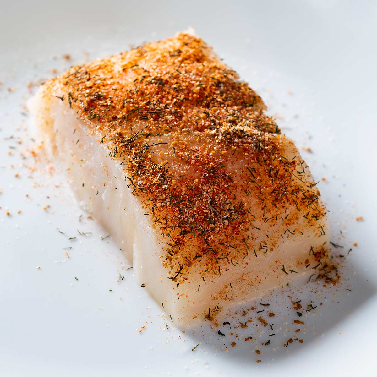 A raw, spice-rubbed cod fillet on a plate.