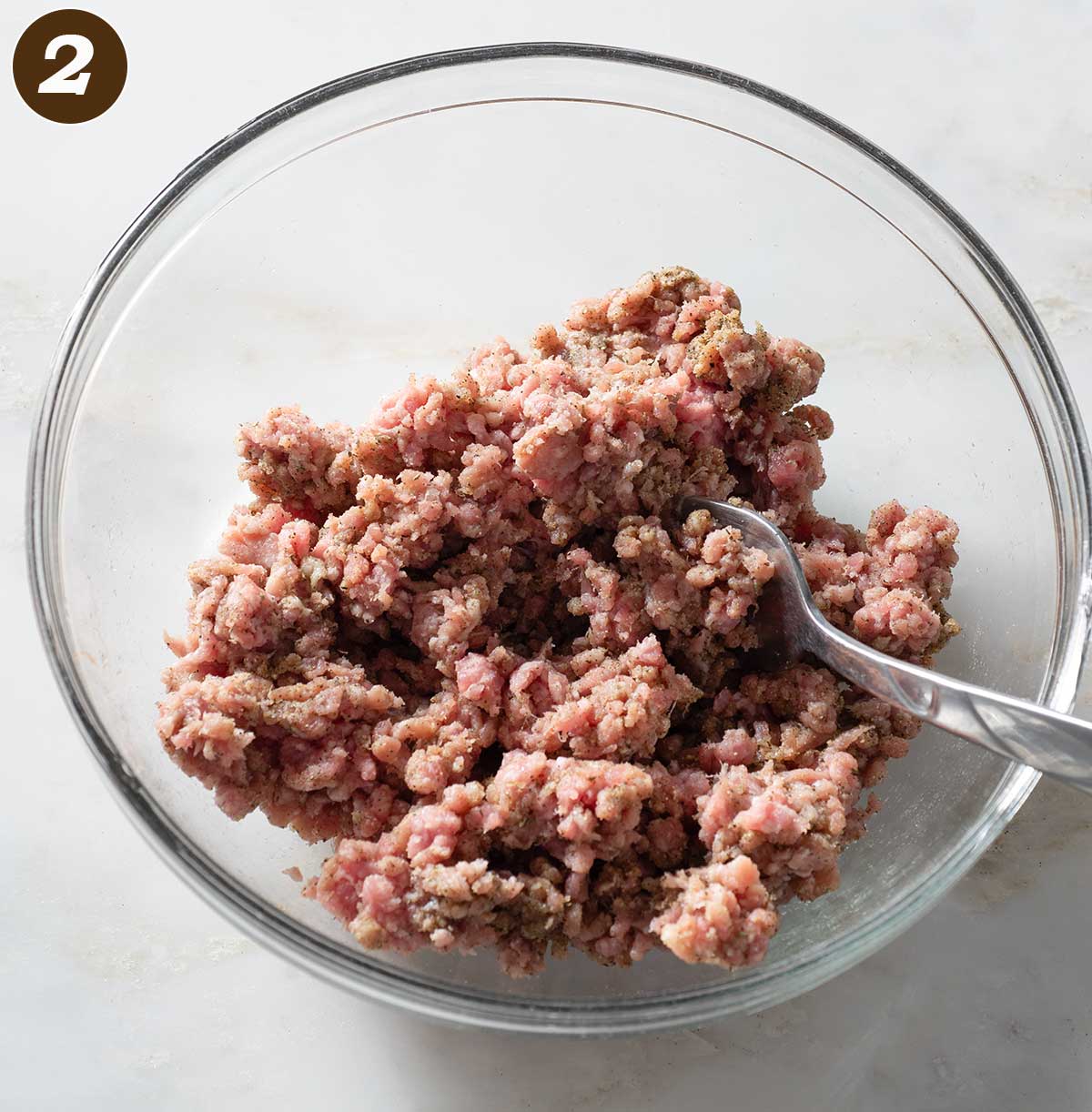 Sausage meat and seasoning being mixed in a bowl.