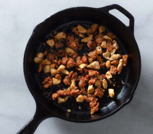Browned chicken and chorizo in a cast iron pan.