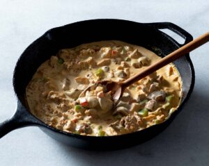 Chicken and chorizo cream sauce being stirred in a cast iron pan.