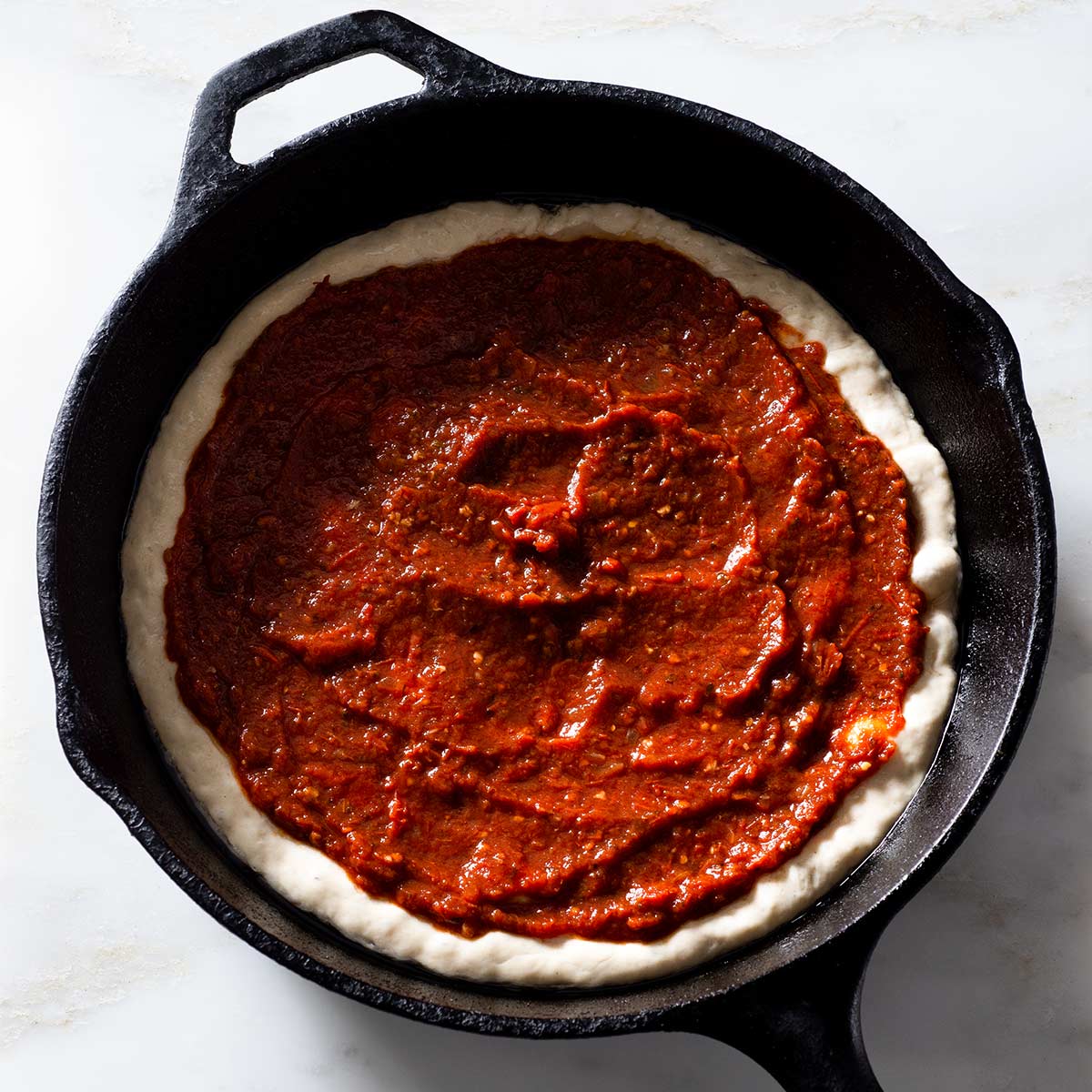 Raw pizza dough with chipotle pizza sauce in a cast iron pan.