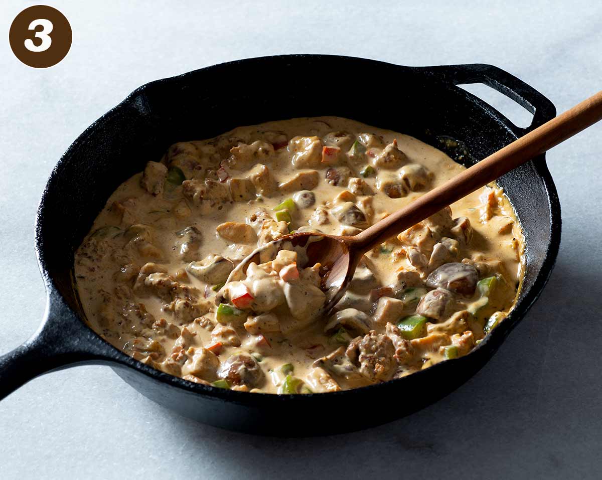 Chicken and chorizo cream sauce being stirred in a cast iron pan.