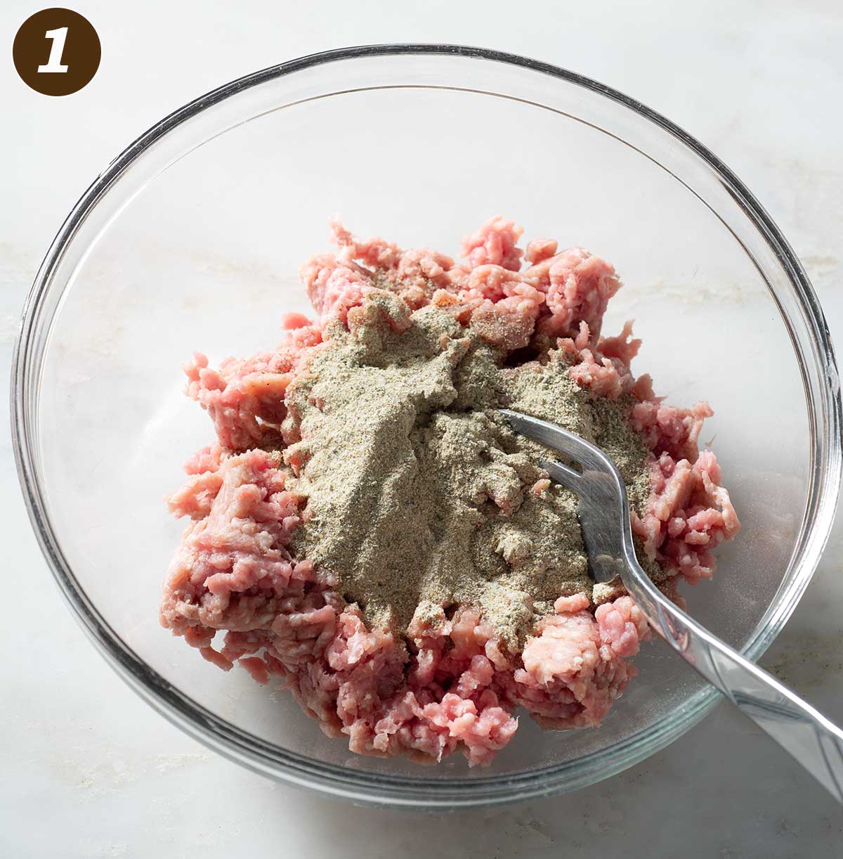 Sausage meat and seasoning in a bowl with a fork.