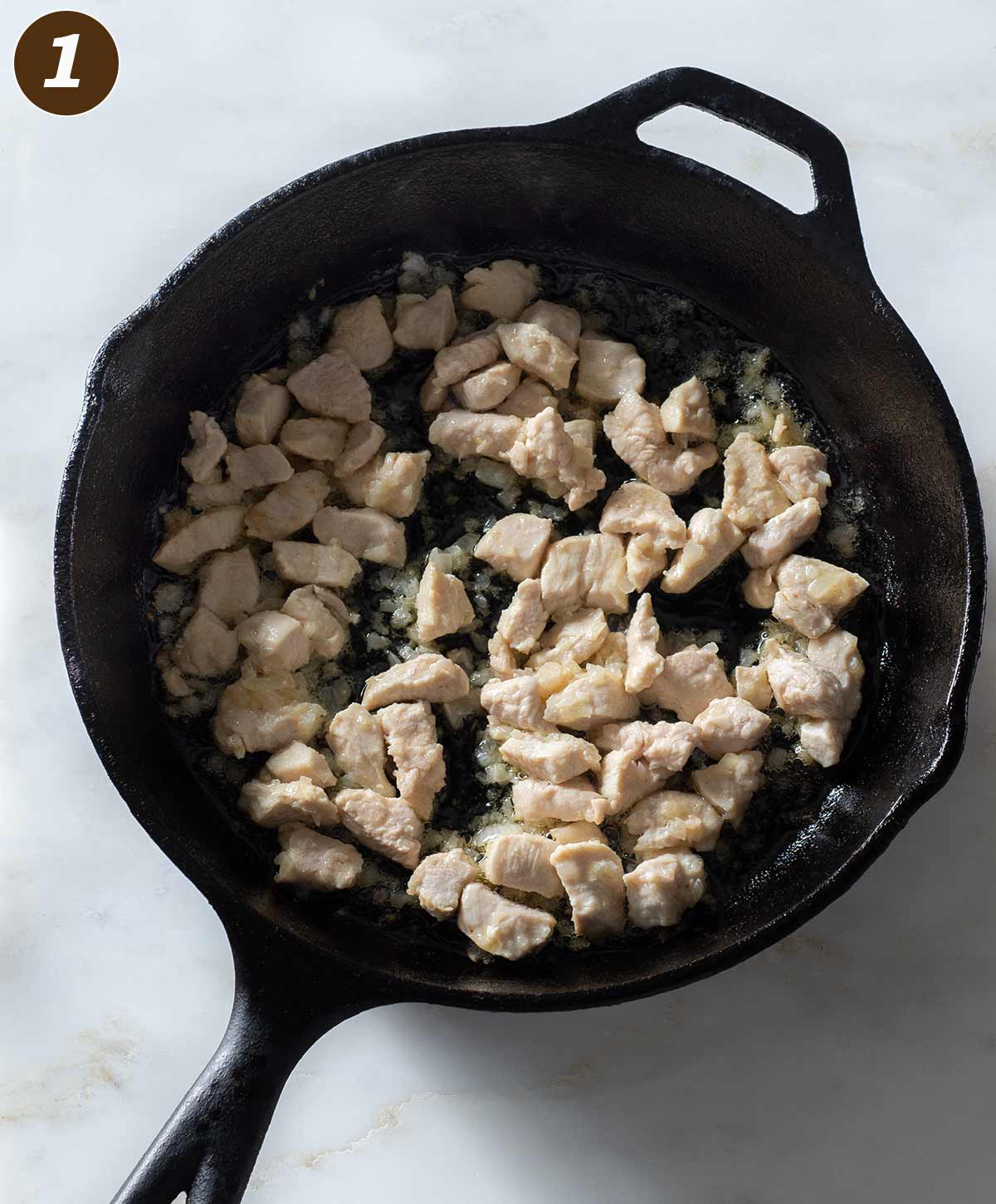 Cooked onion and chicken chunks in a cast iron skillet.