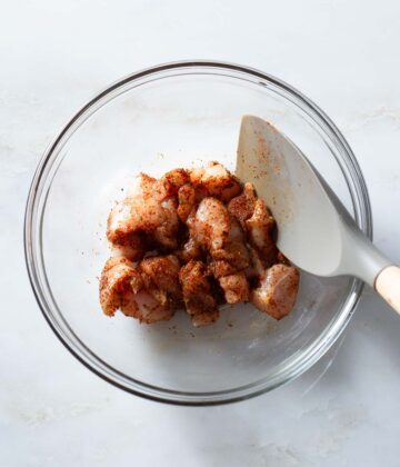 Raw chicken chunks being mixed with seasoning.