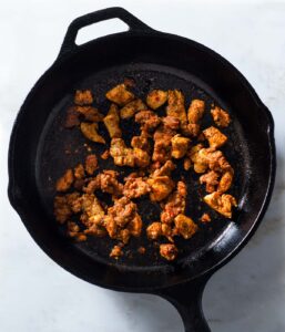 Browned chicken and chorizo in a cast iron pan.