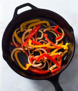 Cooked onion and bell pepper in a cast iron pan.
